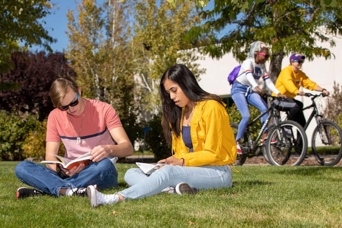 Group of San Juan College students sitting on the grass and two in the back riding bicycles